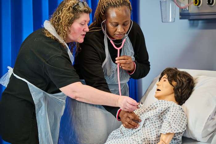 Adult health and social care students treating mannequin in hospital bed