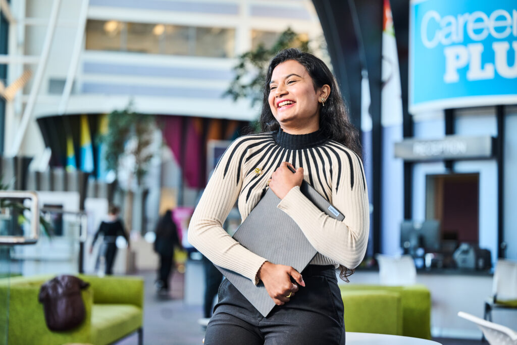 Student with laptop in atrium smiling
